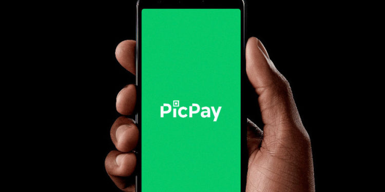 uma mão segurando um celular. A tela é toda verde com o símbolo do PicPay ao centro